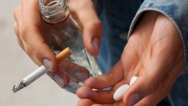 Young woman smoking a cigarette, drinking vodka, and taking pills