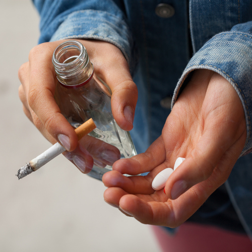Young woman smoking a cigarette, drinking vodka, and taking pills